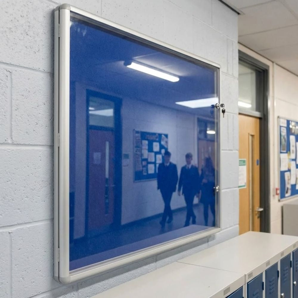 1200 x 1200mm fire resistant tamperproof noticeboard with blue felt surface and aluminium frame, installed in a school corridor with secure glazed door and key locks for protected display.