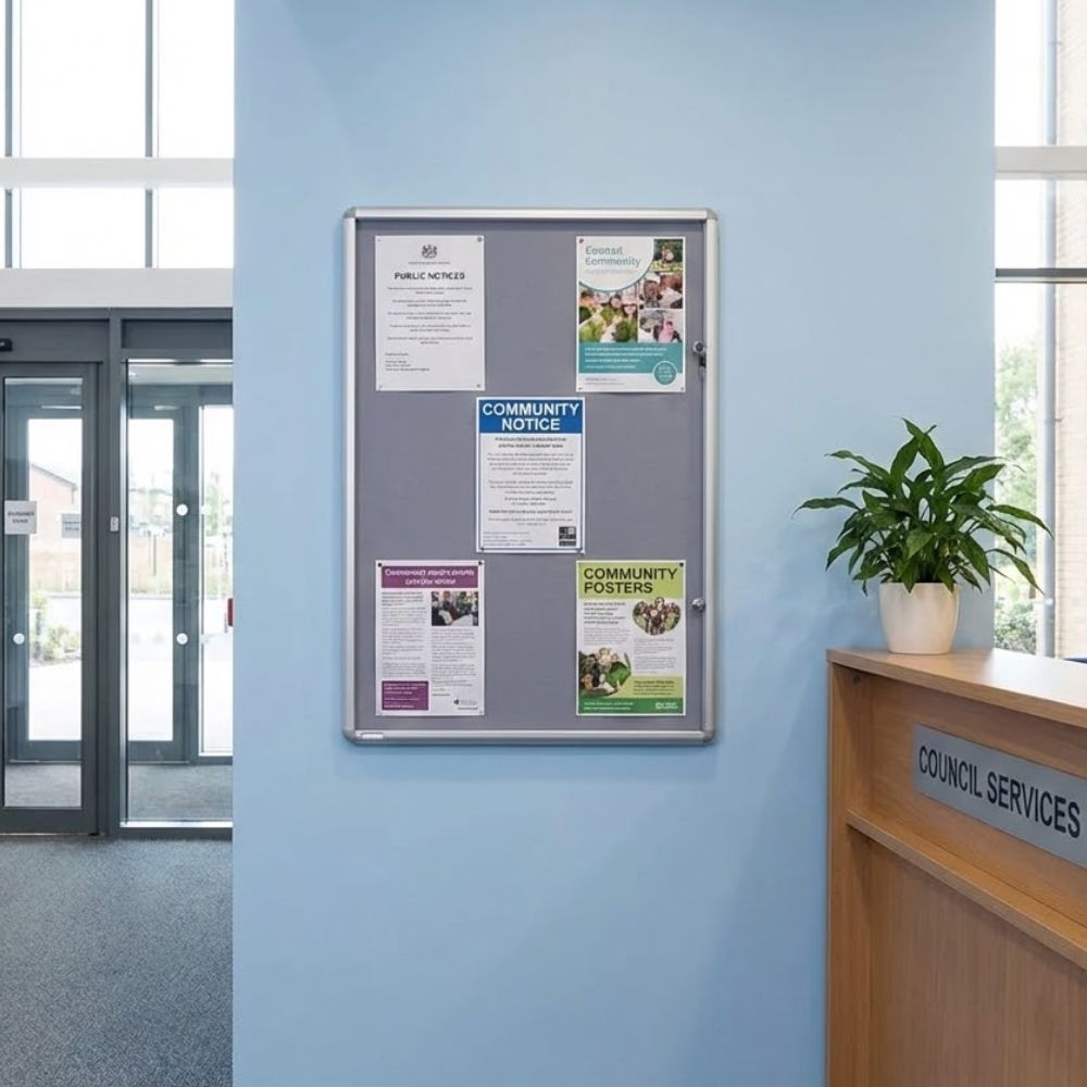 600 x 900mm fire resistant tamperproof noticeboard with grey felt surface and aluminium frame, installed in a council services reception area displaying community notices behind a secure lockable cover.