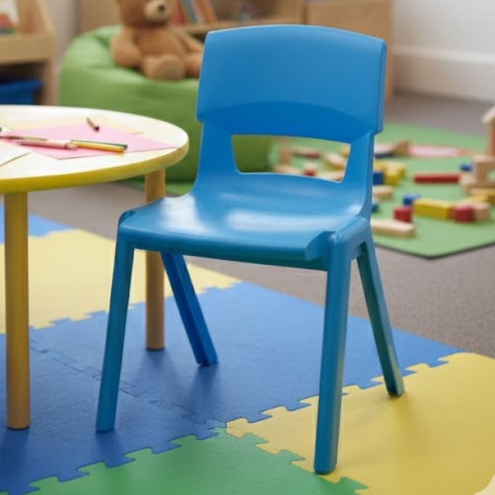 A bright aqua blue chair next to a round activity table in a nursery setting, with colourful foam mats and soft toys arranged for early years play.