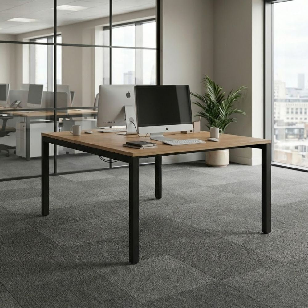 Back-to-back office desk setup with a wood-finish top and black metal legs, featuring dual monitors and minimal workspace accessories in a bright modern office with city views.