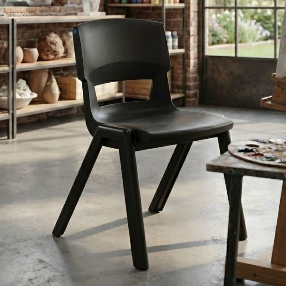 A black plastic art room chair positioned in a creative studio with exposed brick walls, pottery shelves and natural light streaming through large windows.