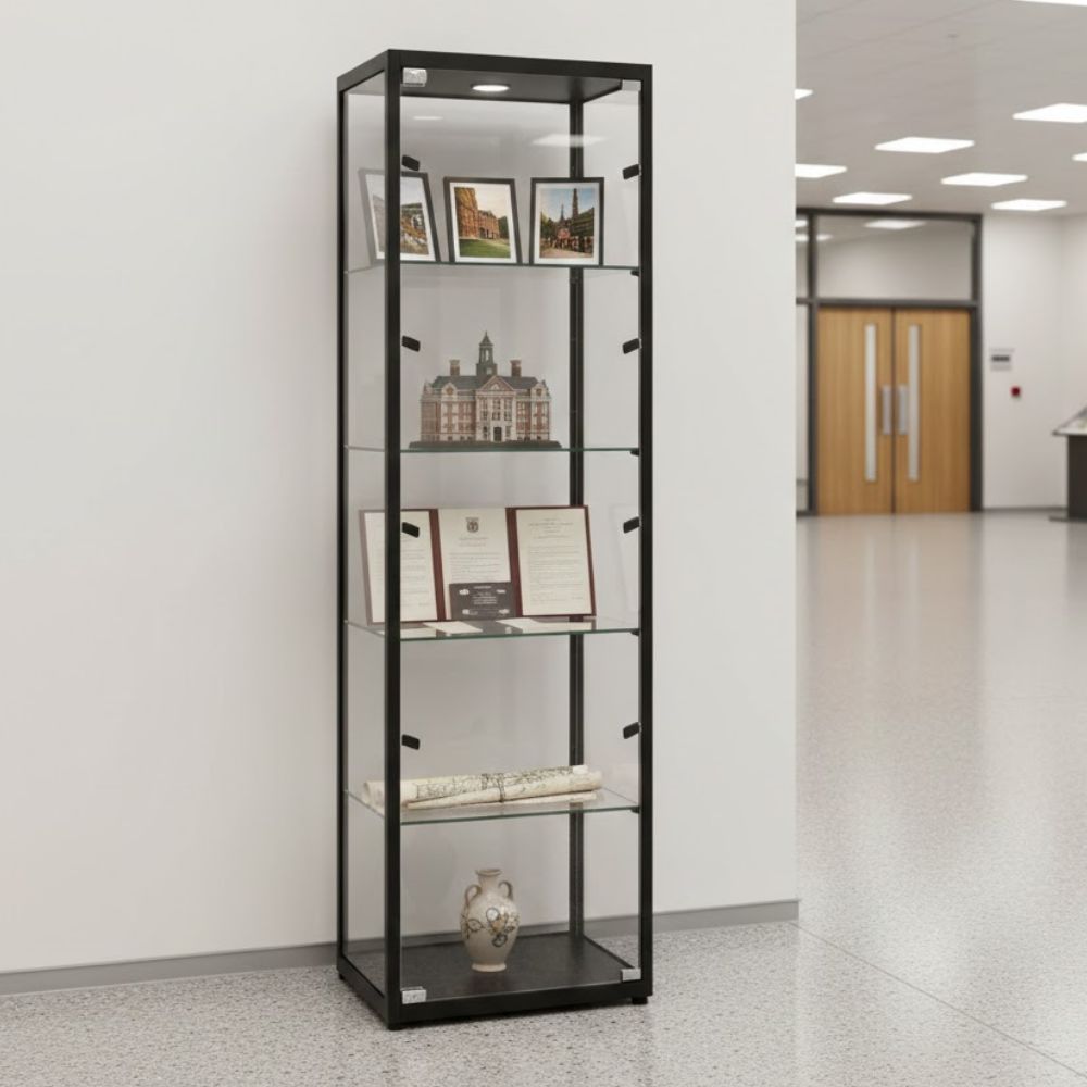 Tall black framed glass display cabinet showcasing framed photographs, certificates, architectural model and decorative artefacts in a modern institutional corridor.