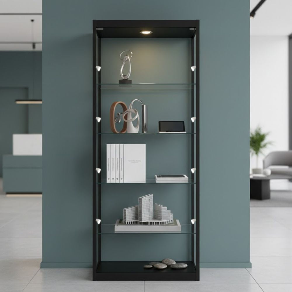Slim black glass display cabinet featuring modern design objects, books and architectural models against a muted green wall in a minimalist interior.