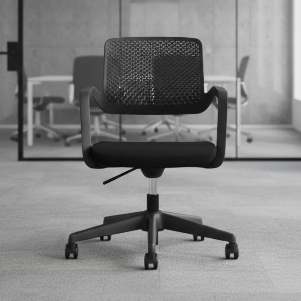 Black swivel office chair with perforated plastic backrest, cushioned seat and five star base with castors, positioned in a contemporary meeting room with glass partition and conference table in the background.