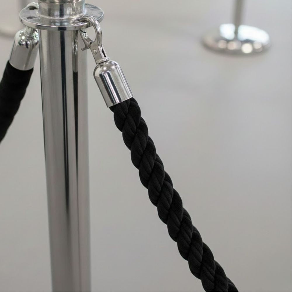 Black twisted rope barrier with polished chrome snap ends attached to a chrome post, commonly used for crowd control, queue management and access restriction in venues such as hotels, theatres, museums, exhibitions and corporate events.