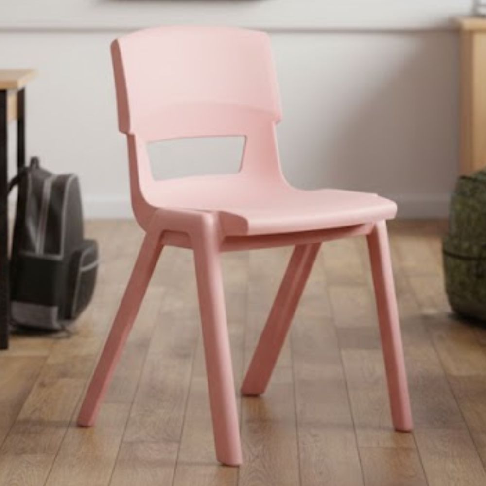 A blush pink plastic learning chair in a modern classroom setting, placed on light wooden flooring with soft furnishings and desk clusters in view.