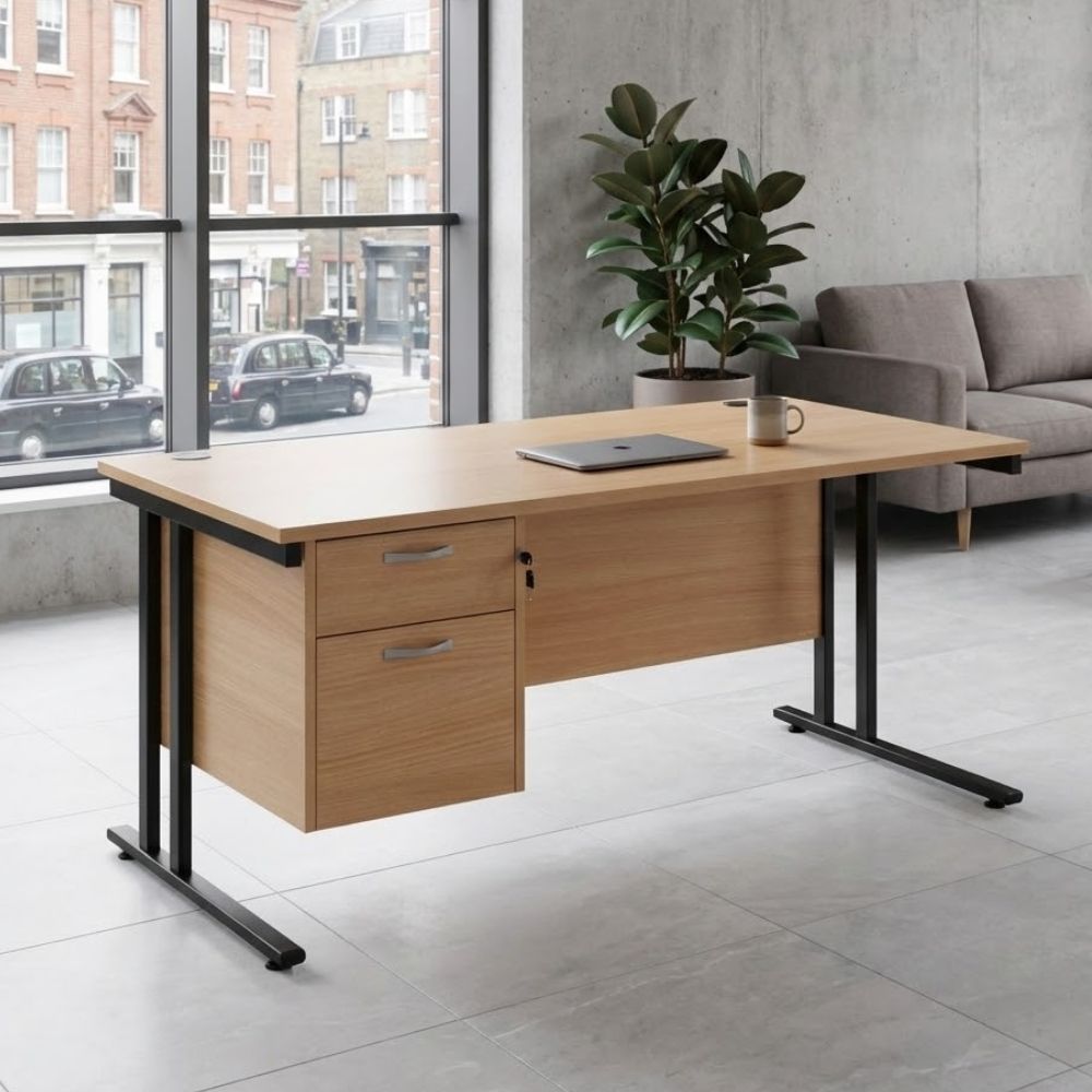 Contemporary office desk with a wood-finish top, two-drawer lockable pedestal, and black cantilever frame, placed in a stylish office with concrete walls and urban views.
