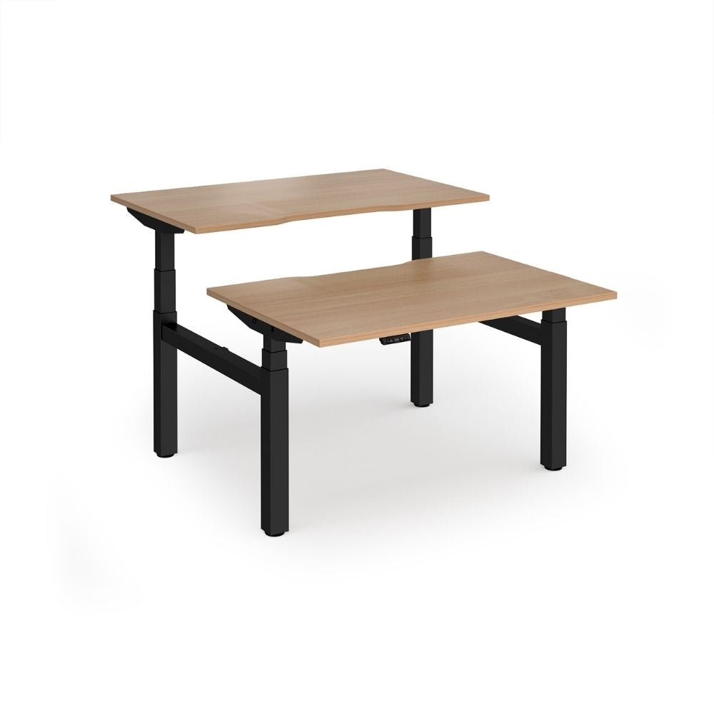 Back-to-back sit-stand desk with dual electric height-adjustable mechanisms, featuring two wood-finish desktops on a shared black frame, ideal for ergonomic office setups.