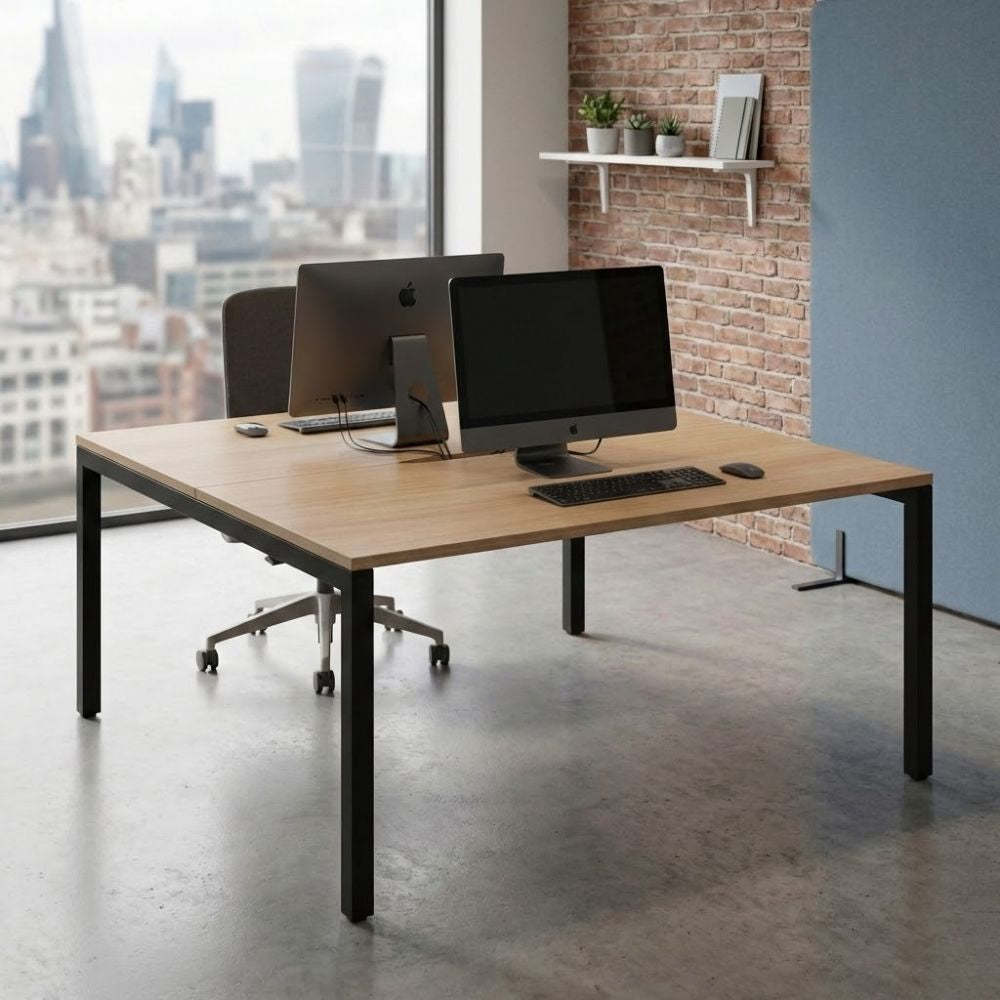 Dual workstation back-to-back office desk with wood-effect tops, black metal frame, and desktop computers, positioned in a city-view office with industrial design features.