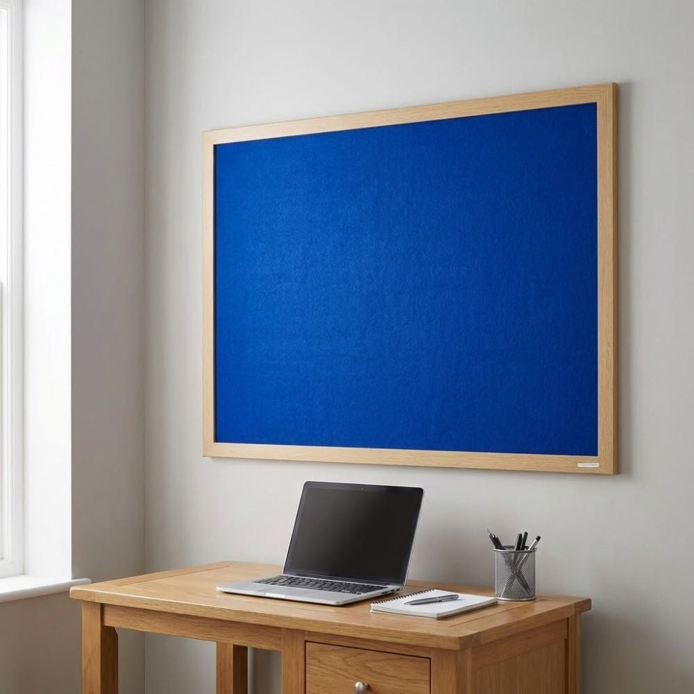 Eco-friendly 900 x 600mm blue felt noticeboard with wood effect frame, wall mounted above a wooden desk with laptop in a modern home office.
