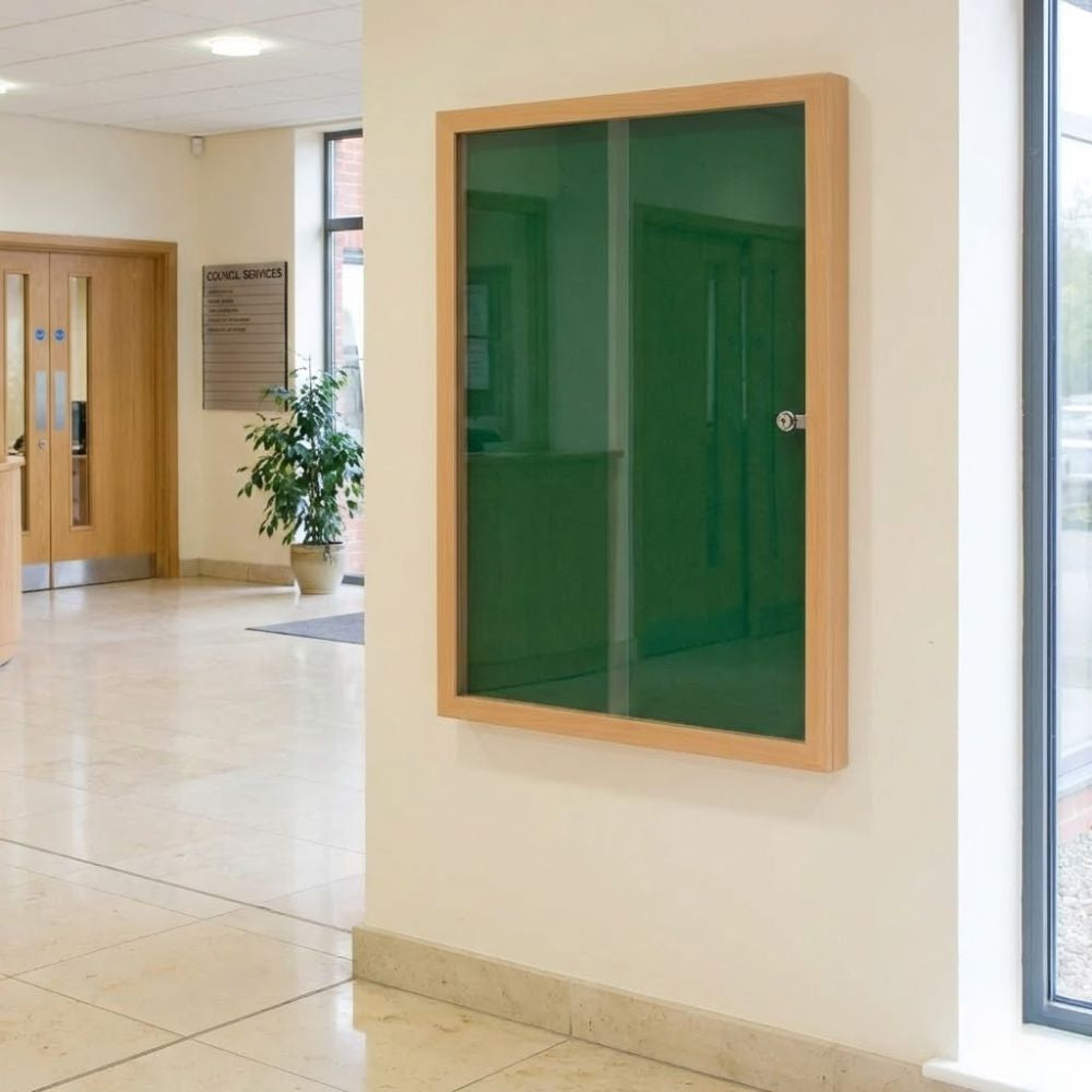 Eco-friendly 900 x 1200mm green felt lockable noticeboard with wood effect frame and clear viewing panel, installed in a public building lobby.
