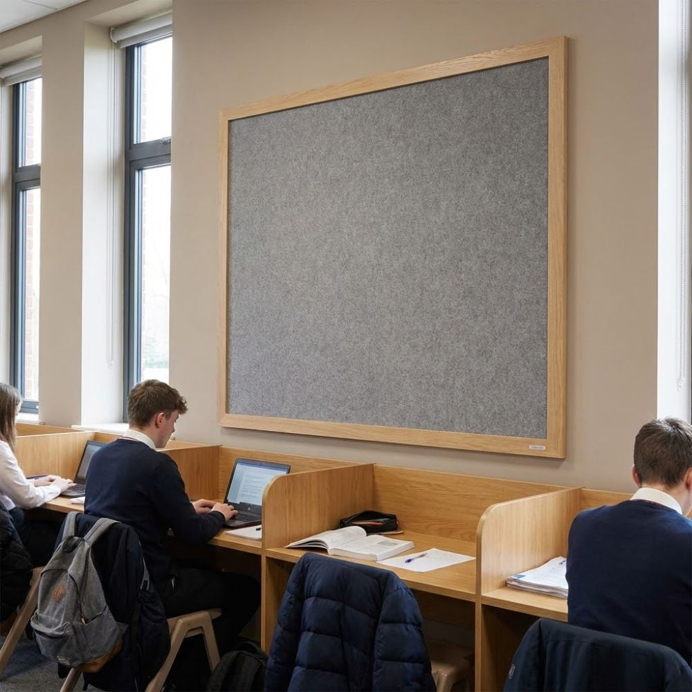 Eco-friendly 1500 x 1200mm grey felt noticeboard with wood effect frame, displayed in a student study area above wooden workstations and laptops.
