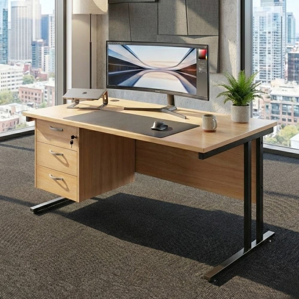Ergonomic office desk setup featuring a three-drawer pedestal, widescreen monitor, and accessories, placed in a high-rise office with city views and acoustic wall panels.