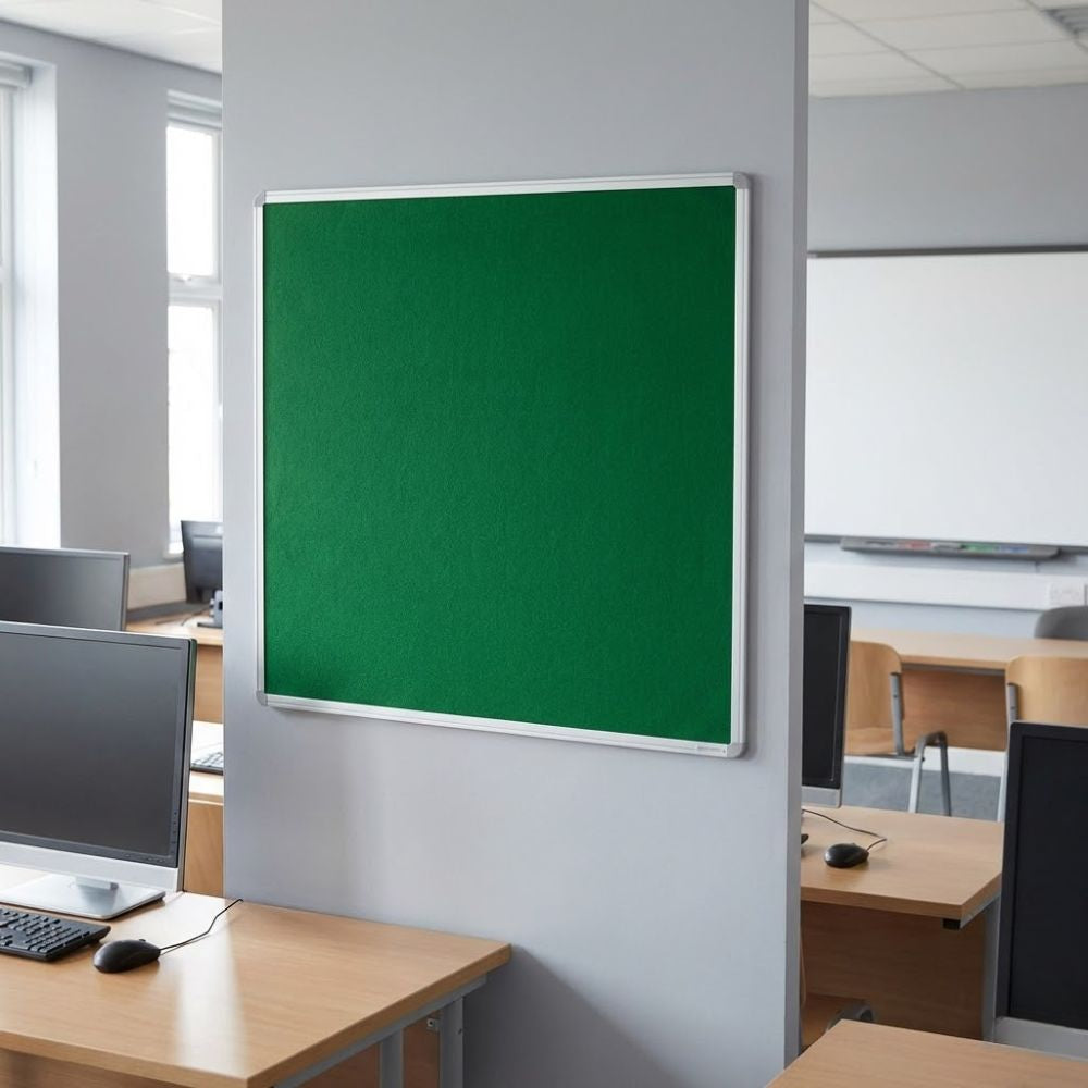 Fire resistant 1200 x 900mm green felt noticeboard with aluminium frame, installed on an office wall between desks and computer workstations.