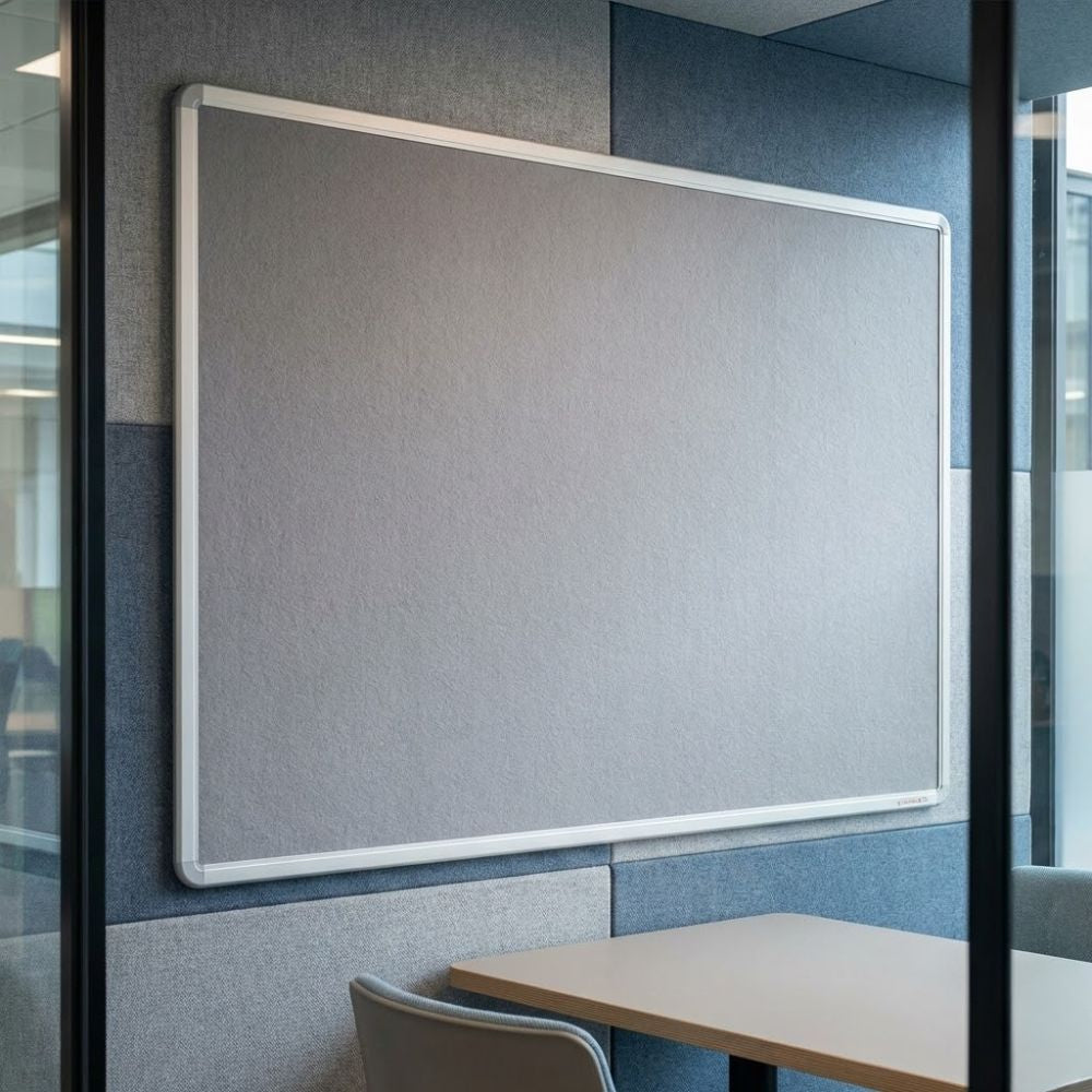 Fire resistant 1200 x 900mm grey felt noticeboard with aluminium frame, mounted in a modern meeting room with upholstered wall panels.