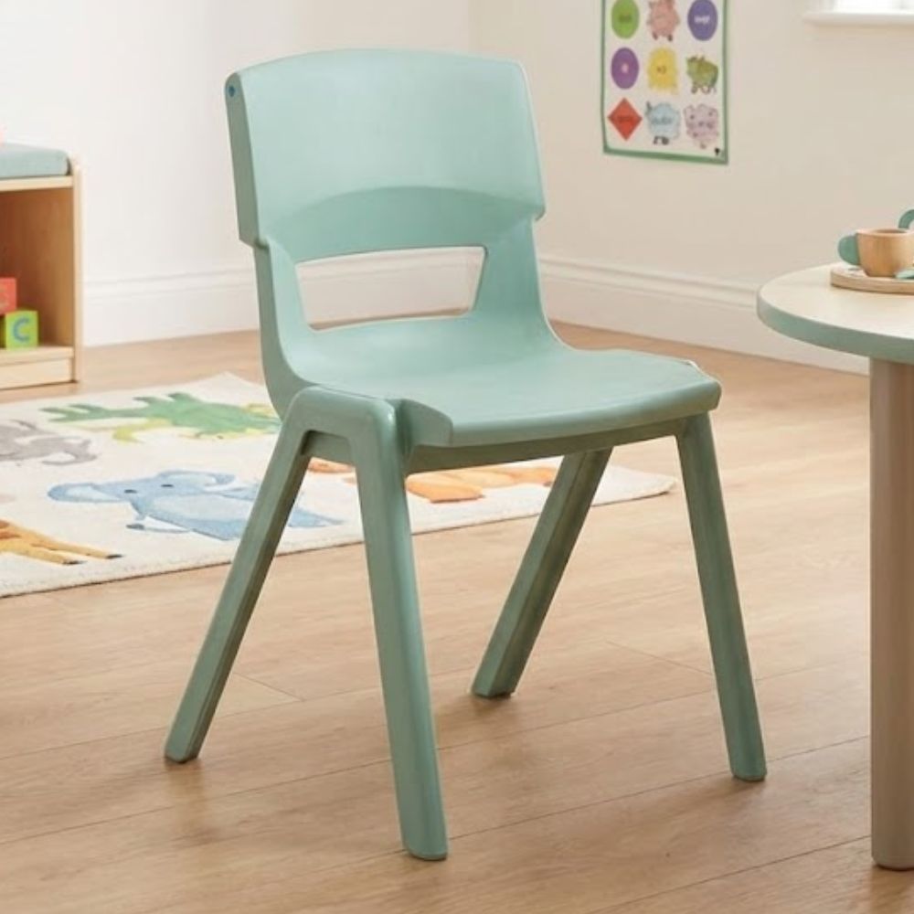 A mint‑green nursery chair with a modern curved backrest, placed beside a circular activity table in a light-filled classroom with playful animal-themed décor.