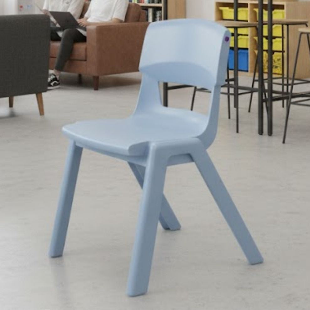 A pale blue plastic school chair positioned in a contemporary classroom with light flooring and collaborative seating areas in the background.