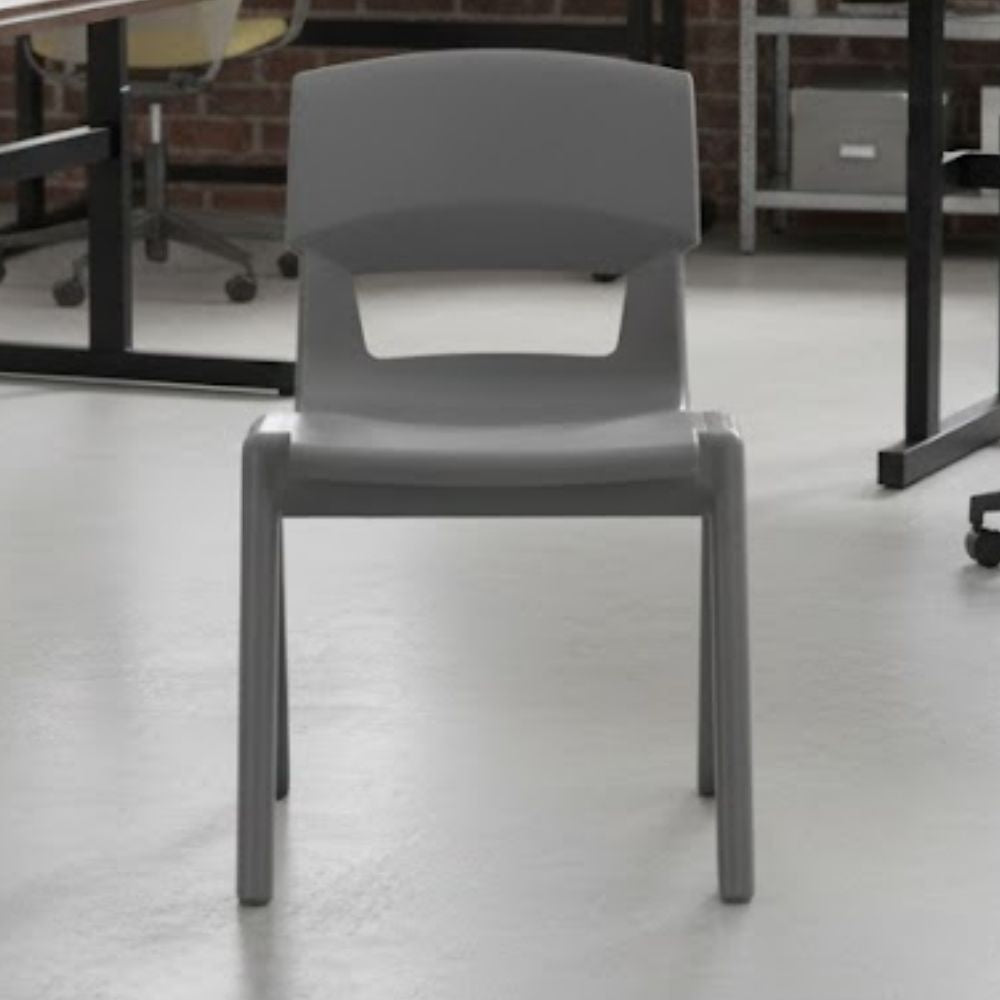 A mid-grey plastic chair positioned in a bright, industrial-style classroom with clean white flooring and exposed brickwork, ideal for creative education environments.