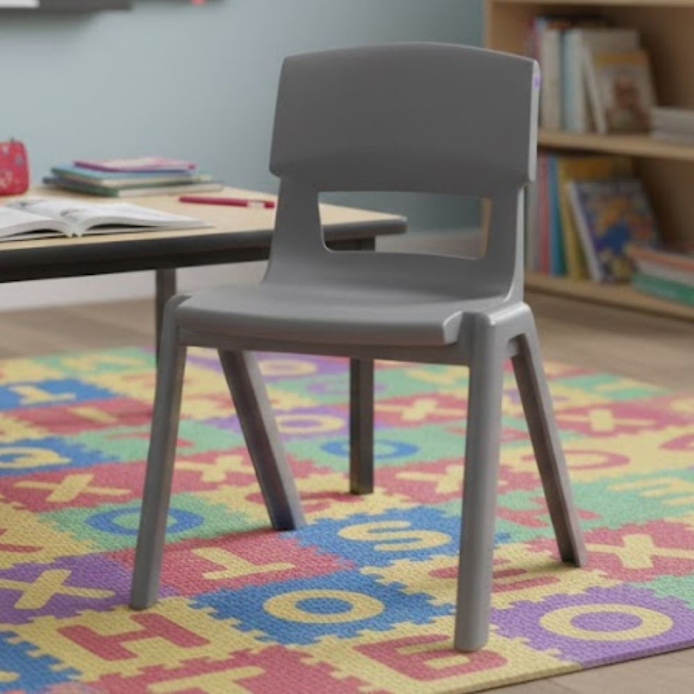 A mid-grey children’s learning chair on a colourful alphabet-themed rug in a phonics-based classroom, with low activity tables and well-stocked book displays.