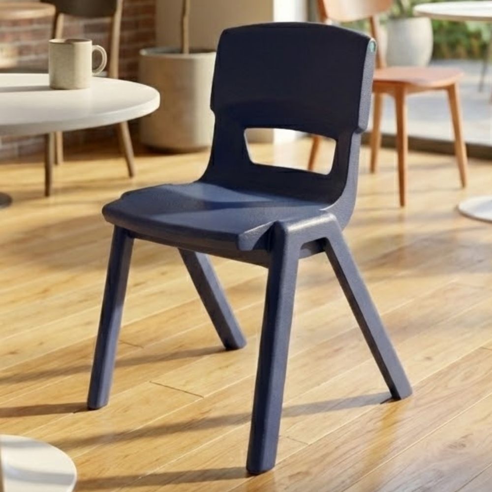 A navy blue plastic chair placed in a school breakout space with café-style tables and wooden floors, ideal for informal study and group discussions.