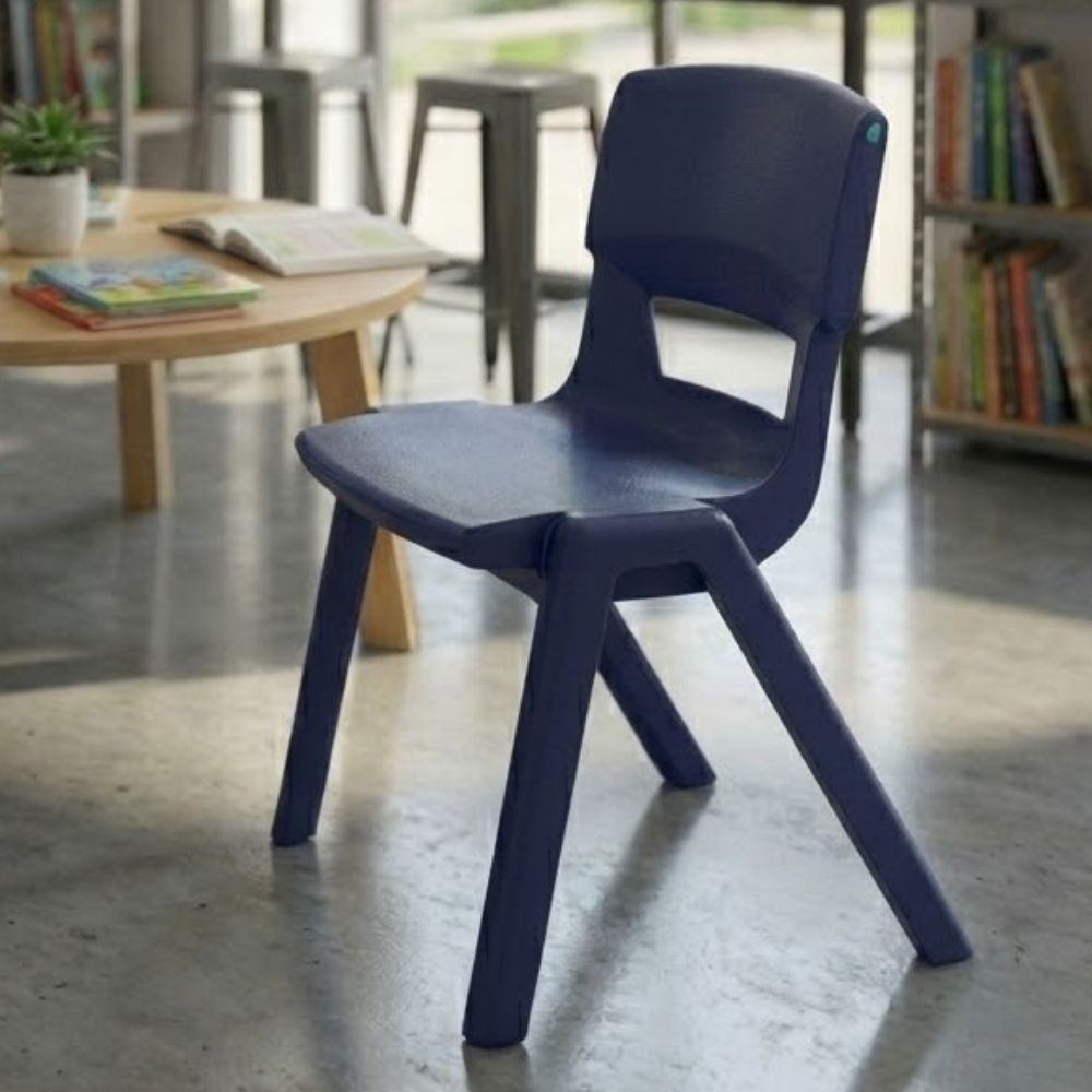 A navy blue ergonomic chair in a contemporary library study area, set on polished concrete flooring near bookshelves and a wooden round table.