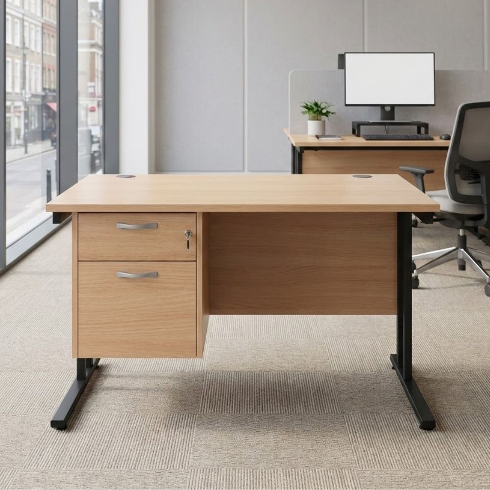Wooden office desk with a two-drawer lockable pedestal, black cantilever legs, and modesty panel, set in a bright modern workspace with floor-to-ceiling windows.