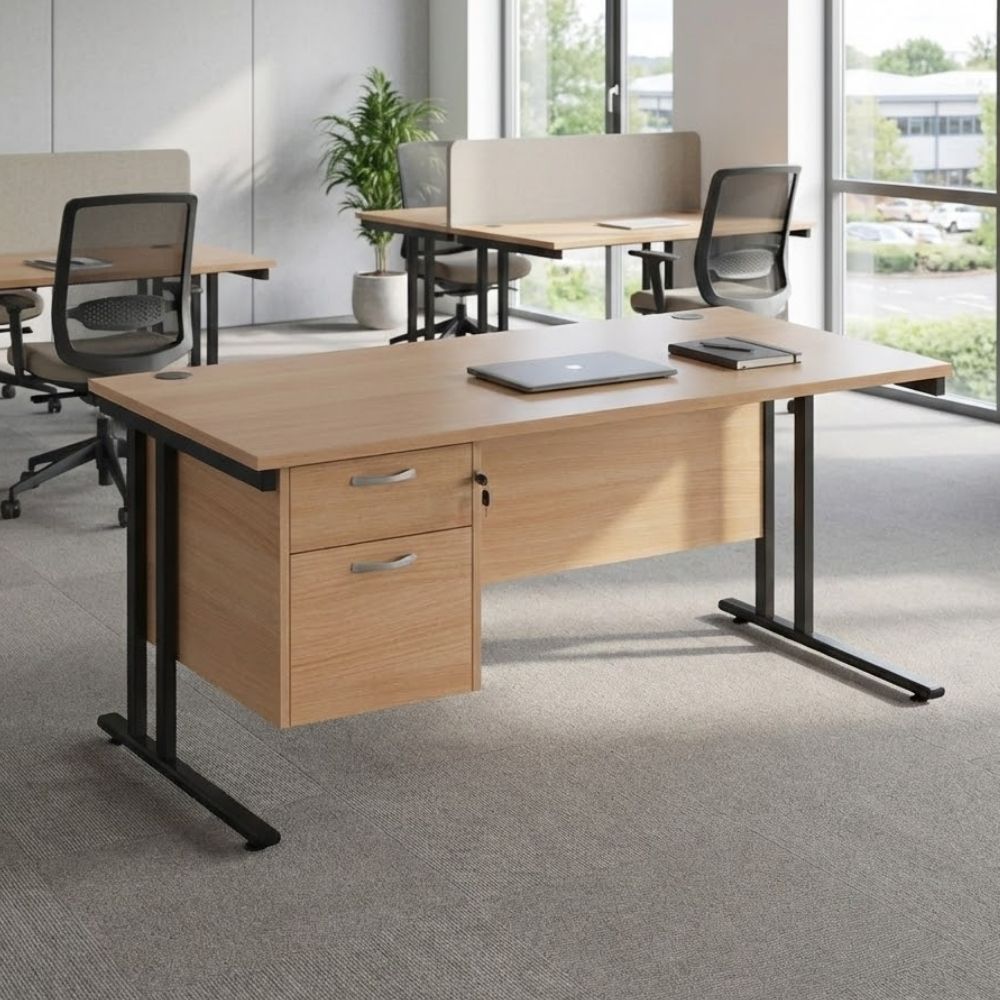 Office workstation with a wooden top, black cantilever legs, and two-drawer pedestal, shown with a laptop and notebook, in a bright collaborative workspace with window views.