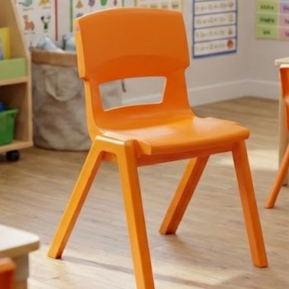 An orange plastic nursery chair on warm wood flooring, set in a classroom decorated with colourful educational posters and play storage.