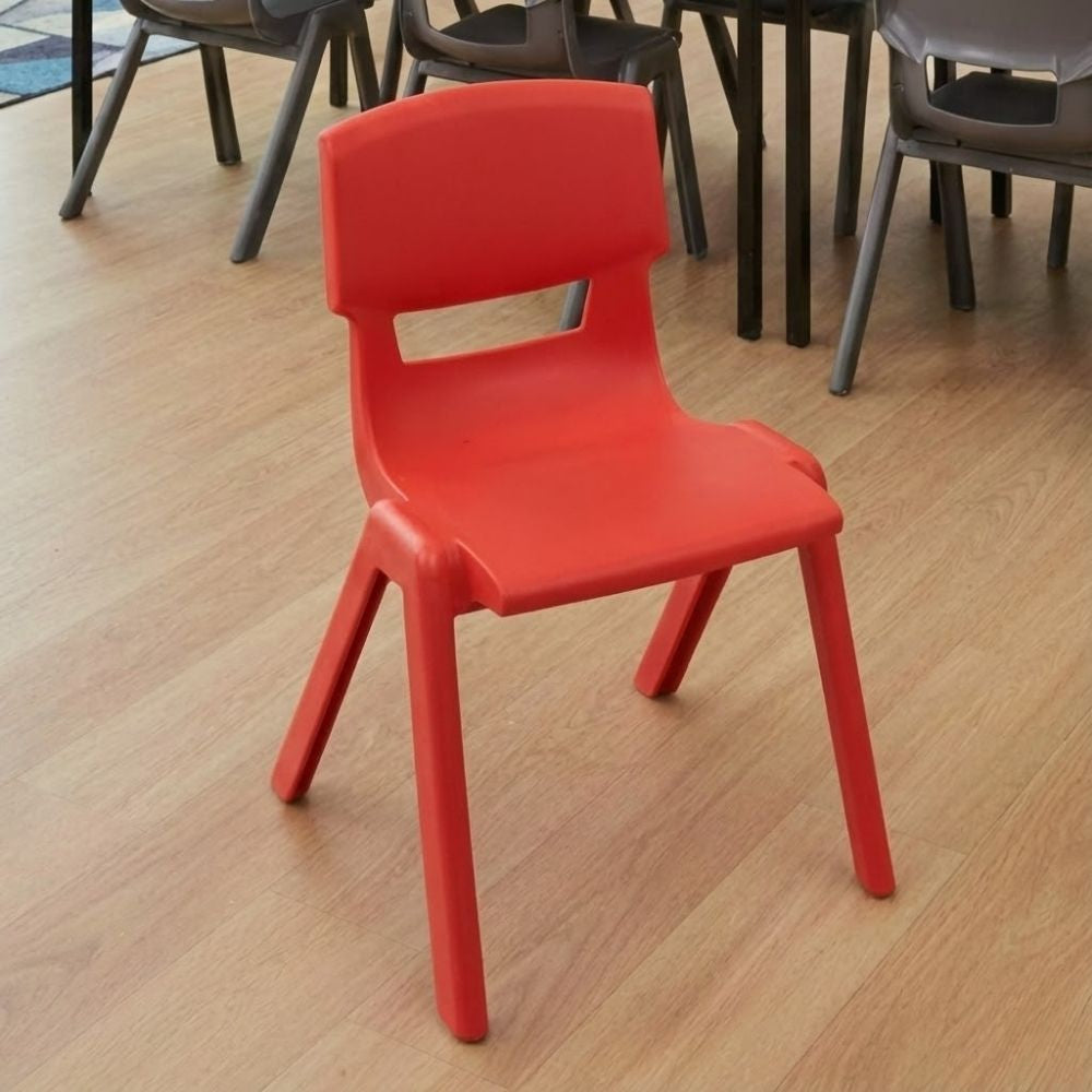 A red plastic school chair situated in a classroom with a wooden floor, grouped around a table with grey chairs for collaborative learning.