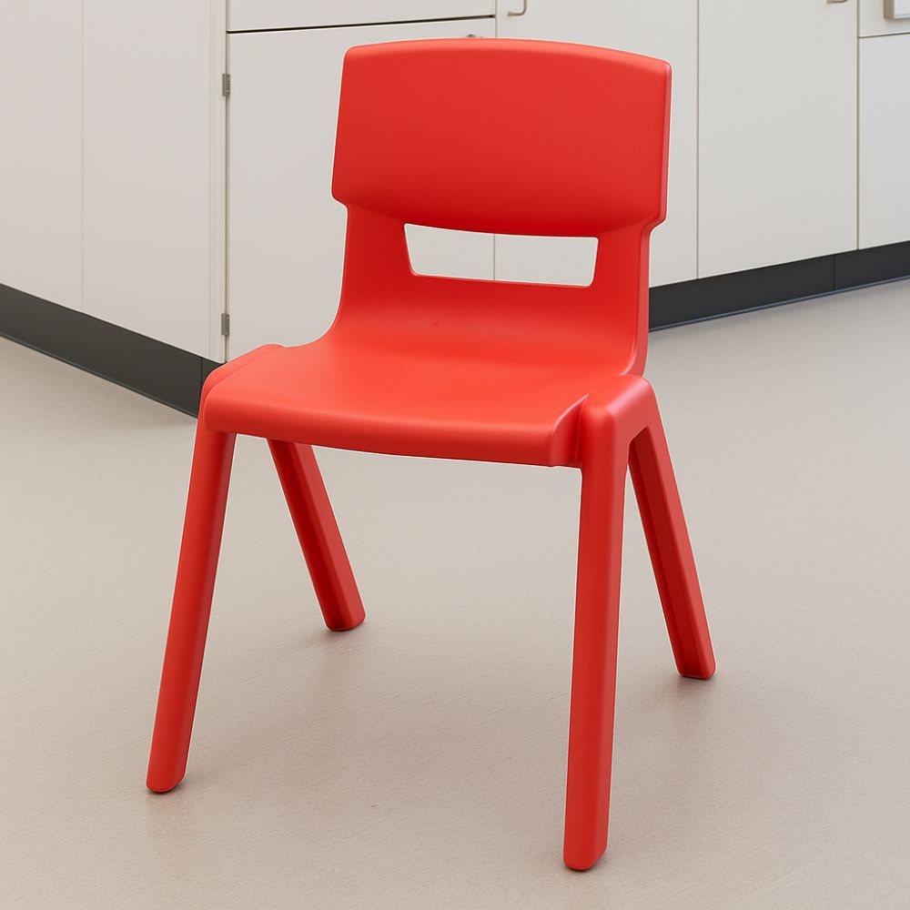 A red classroom chair with a contoured seat and angled legs, positioned in a school room with light flooring and white cupboards.