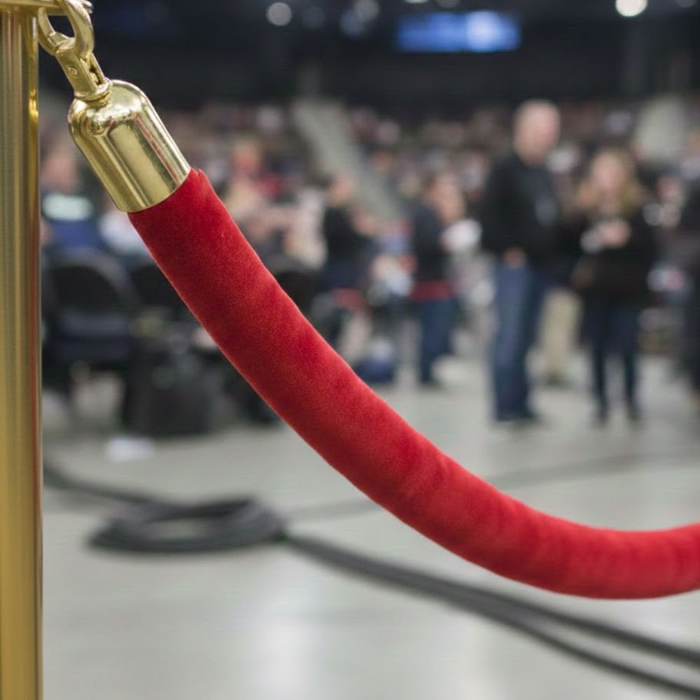Red-velvet-rope-attached-to-gold-barrier-post-with-audience-and-stage-area-blurred-in-background