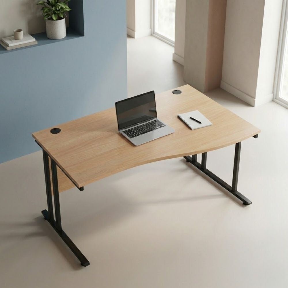 Contemporary right-hand wave desk featuring a wooden top and black leg frame, placed in a bright minimalist office space with soft natural light and simple decor.