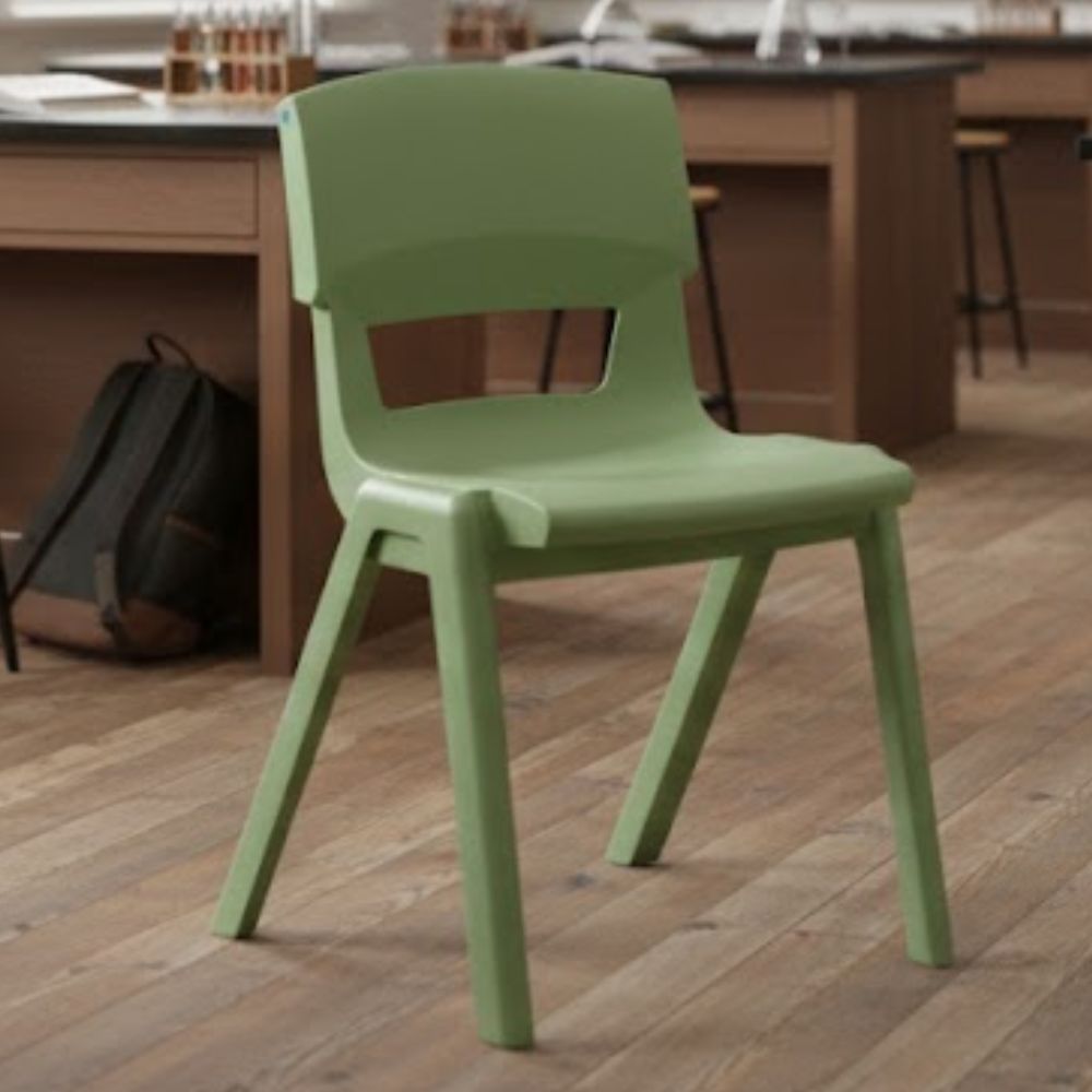 A sage green ergonomic classroom chair set on warm wood flooring in a science lab, with wooden workbenches and backpacks in the background.