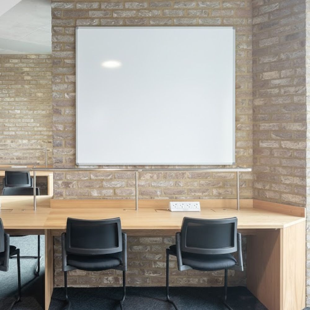Wall-mounted whiteboard with metallic frame above a dual-desk setup, designed for collaborative study or workspaces.