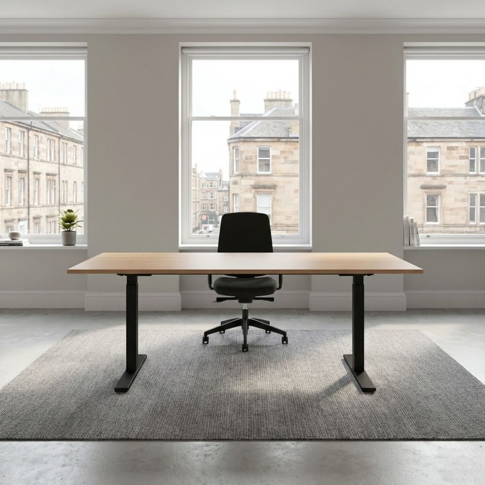 Spacious electric height-adjustable desk with a wood-effect top and black metal frame, positioned on a grey rug in a bright traditional-style office with sash windows.