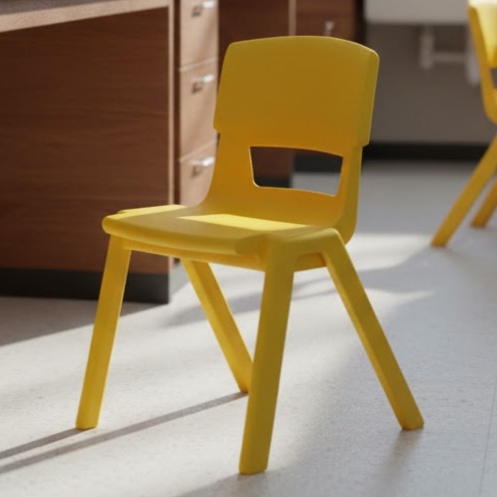 A bright yellow plastic school chair placed in a sunlit classroom beside wooden cabinets and a clean, pale floor.